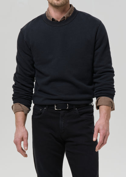 Person wearing a black crewneck sweatshirt with black straight leg jeans on a grey background.