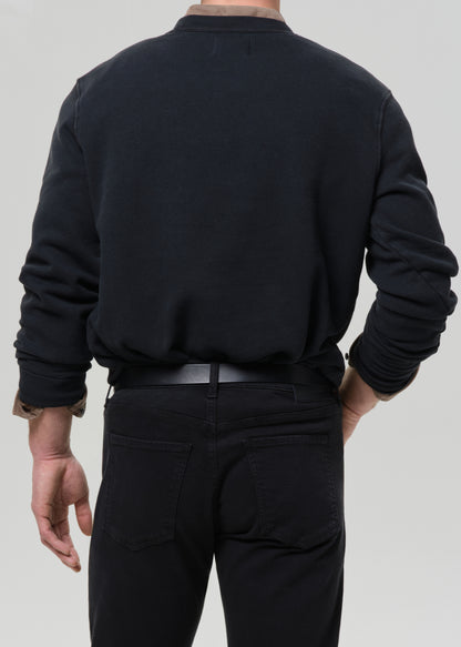 Person wearing a black crewneck sweatshirt with black straight leg jeans viewed from the back on a grey background.