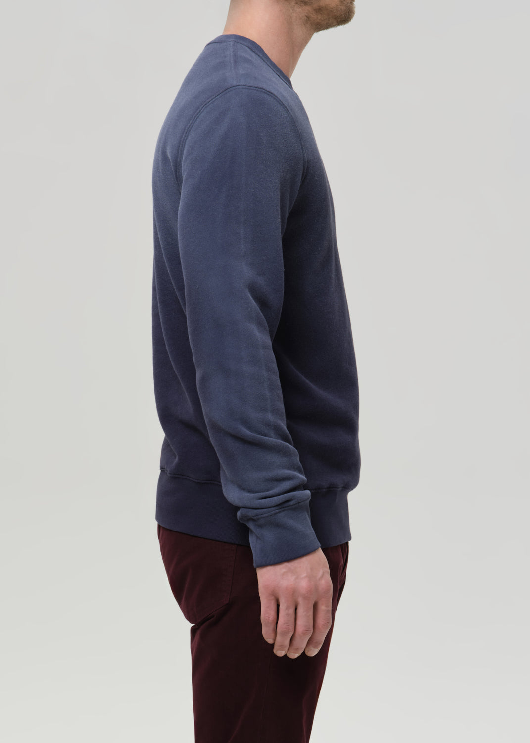 Person wearing a blue sweater and maroon pants on a grey background