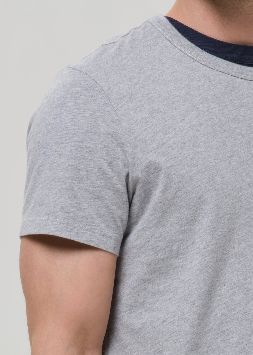 Close-up of a person wearing a light heather grey short-sleeve t-shirt with a contrasting dark navy blue crew neck.