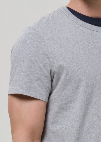 Close-up of a person wearing a light heather grey short-sleeve t-shirt with a contrasting dark navy blue crew neck.