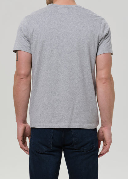 A man viewed from the back wearing a light grey heather crewneck t-shirt and dark blue jeans, set against a grey background.