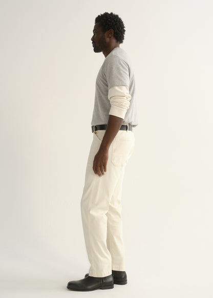 Person wearing a light grey crewneck t-shirt with cream trousers and black shoes, side full body view on a light grey background.