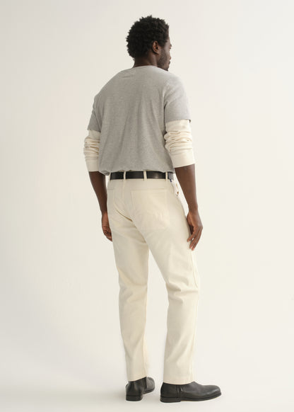 Person wearing a light grey crewneck t-shirt with cream trousers and black shoes, back full body view on a light grey background.