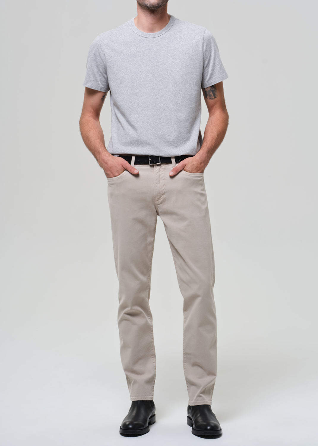 Man wearing a gray t-shirt, beige pants, and black shoes on a white background