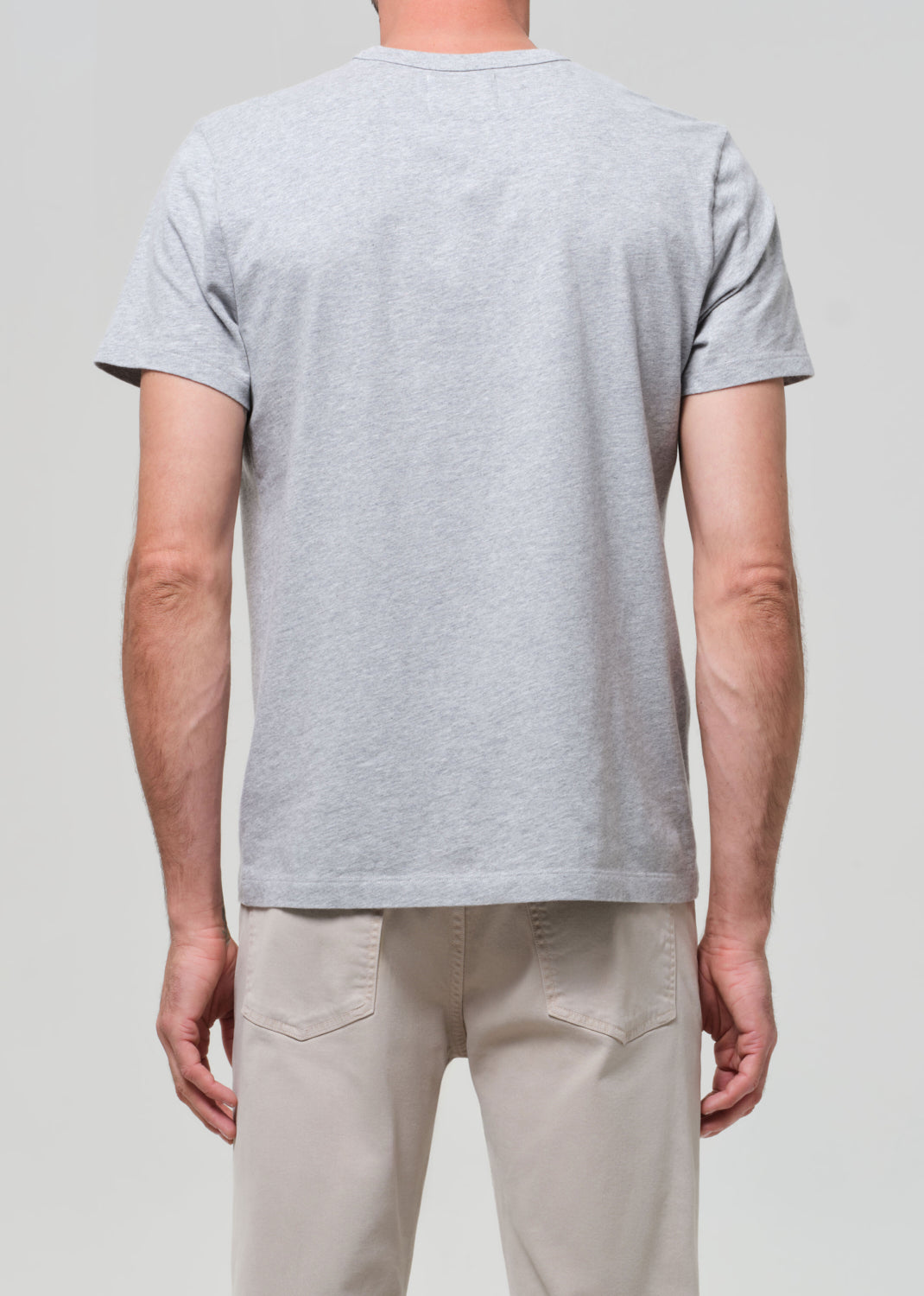 Person wearing a gray t-shirt and beige pants against a plain background