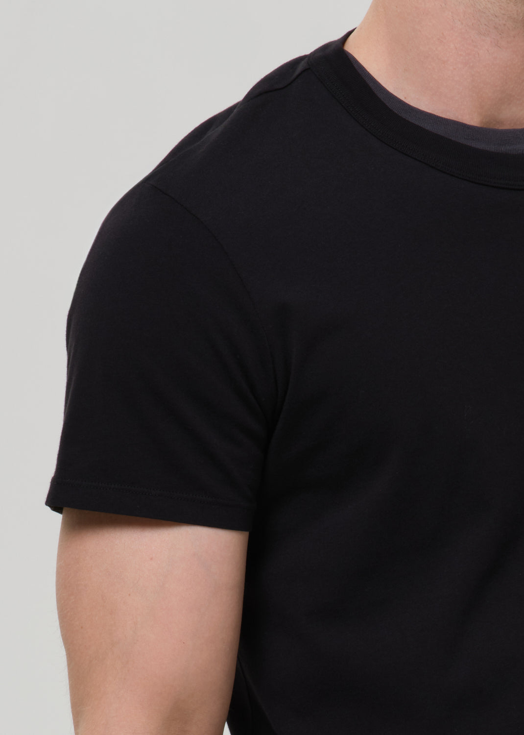 Close-up of a person wearing a plain black short-sleeve crew-neck t-shirt against a grey background.