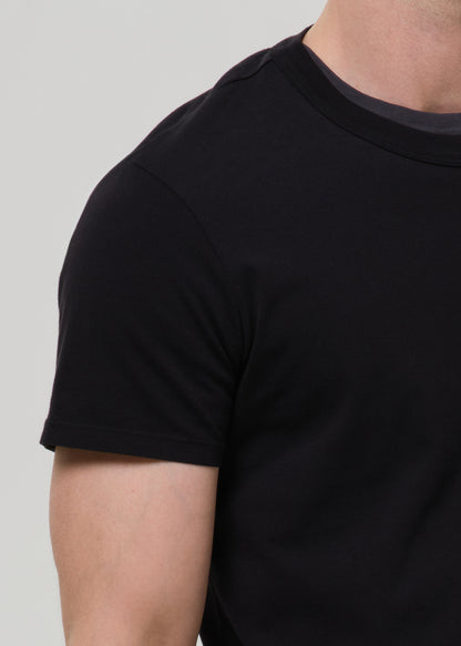 Close-up of a person wearing a plain black short-sleeve crew-neck t-shirt against a grey background.
