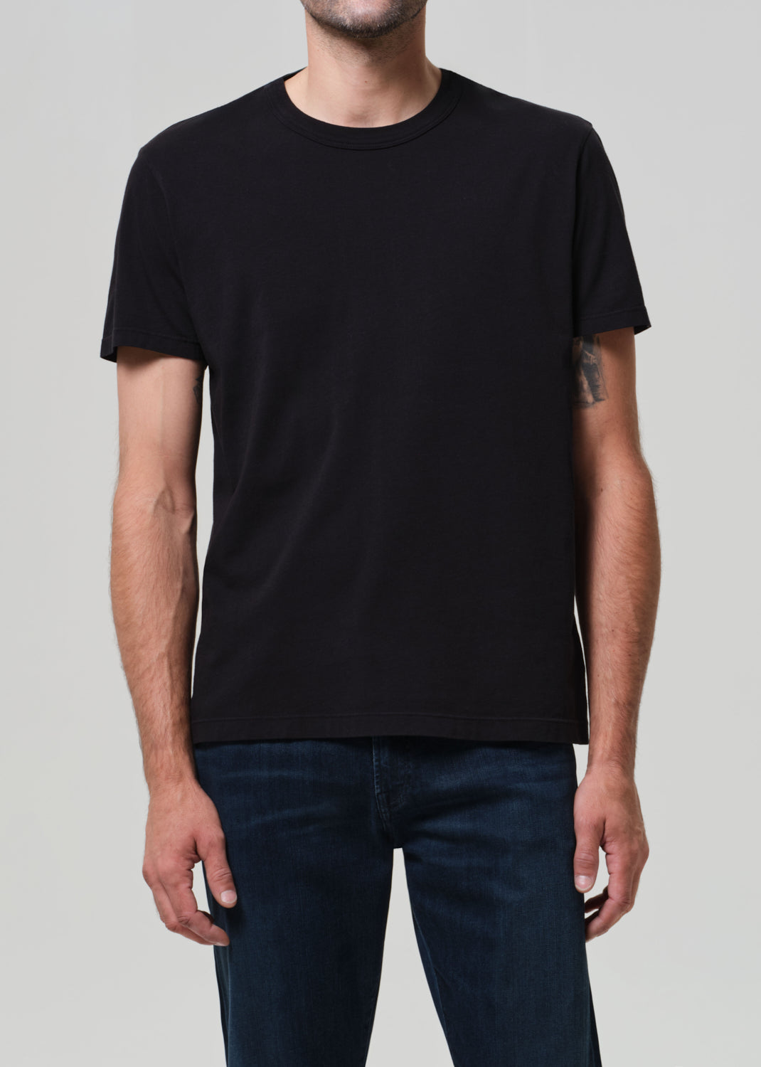 Person wearing a plain black t-shirt and dark jeans on a light gray background