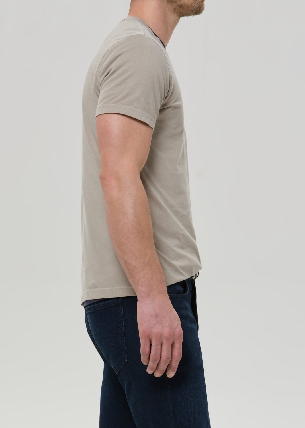 Man wearing a beige t-shirt and dark pants on a light gray background