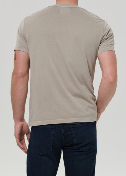 Person wearing a beige t-shirt and dark pants on a plain background