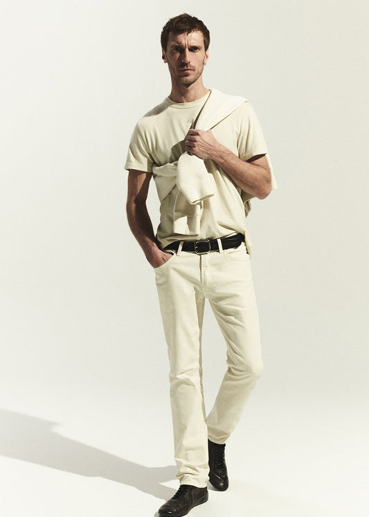 Man wearing a light-colored t-shirt and pants holding a folded shirt against a white background