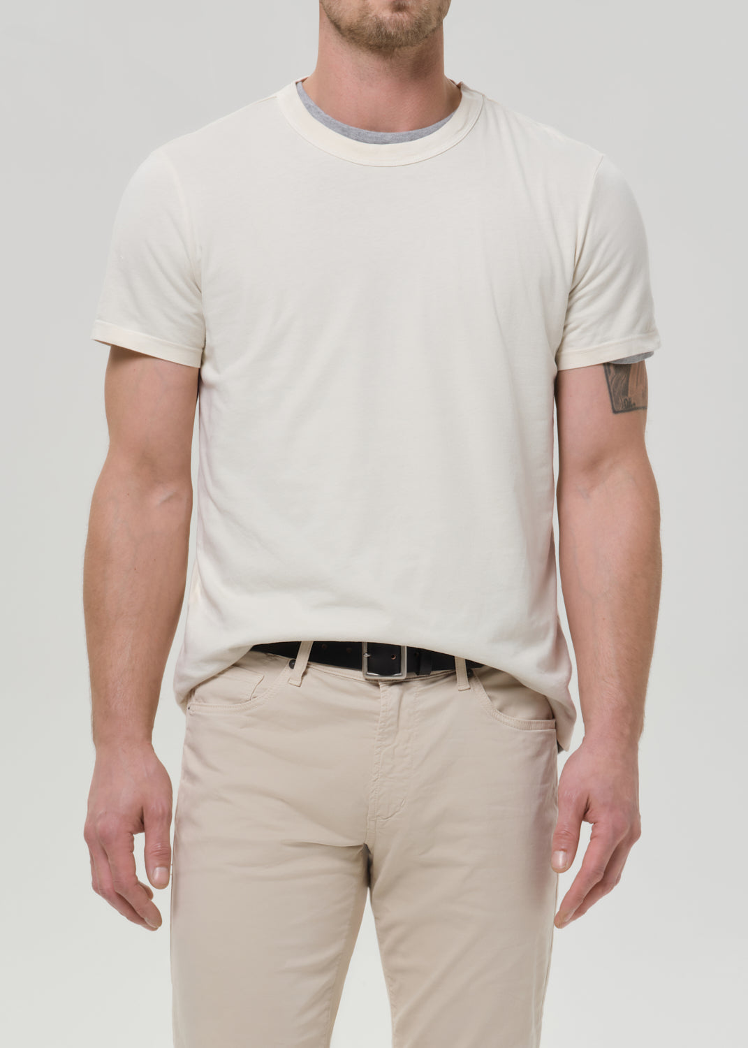 Person wearing a cream crewneck short sleeve tee with light beige straight leg pants on a grey background.