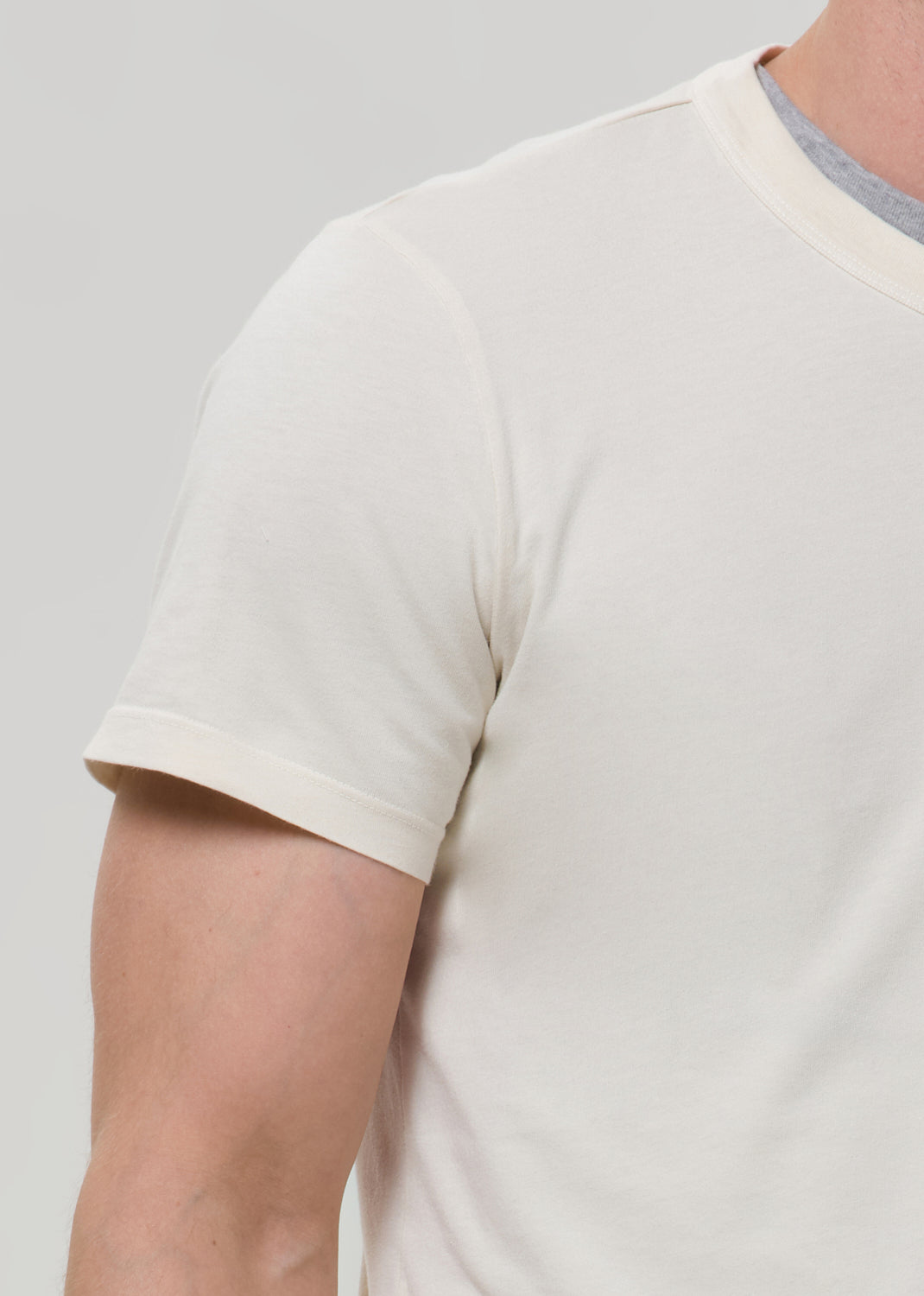 Close-up of a cream crewneck short sleeve tee on a grey background.