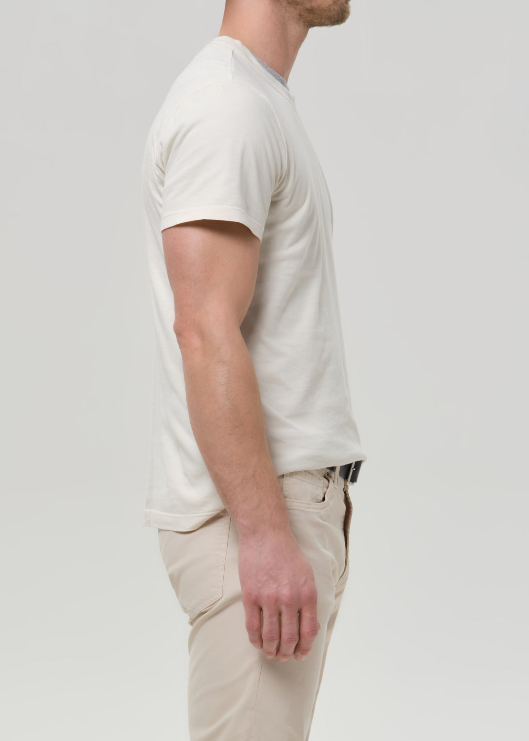 Person wearing a cream crewneck short sleeve tee with light beige straight leg pants viewed from the side on a grey background.