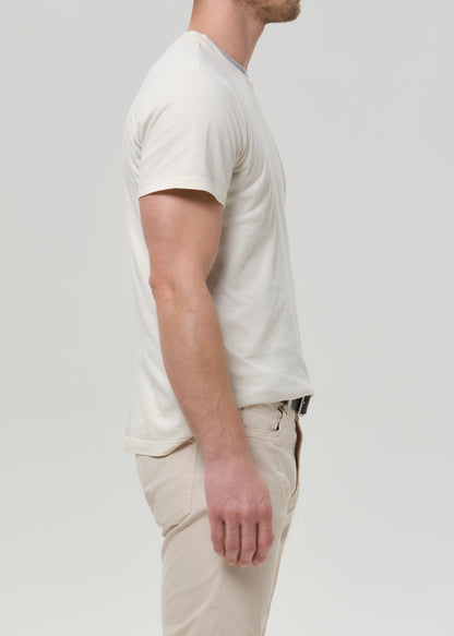 Person wearing a cream crewneck short sleeve tee with light beige straight leg pants viewed from the side on a grey background.
