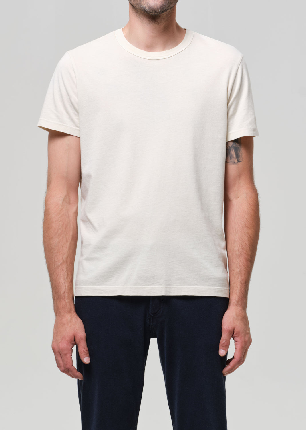 Person wearing a plain cream t-shirt and navy jeans on a light gray background