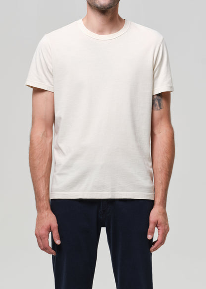 Person wearing a plain cream t-shirt and navy jeans on a light gray background