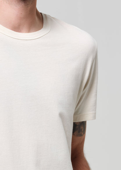 Person wearing a plain cream t-shirt and navy jeans on a light gray background