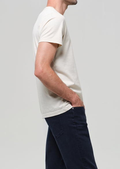 Person wearing a plain cream t-shirt and navy jeans on a light gray background