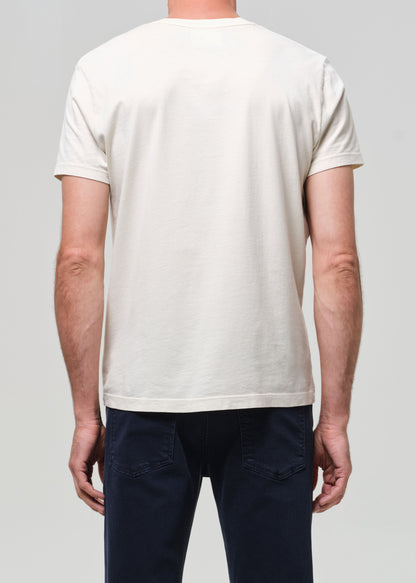 Person wearing a plain cream t-shirt and navy jeans on a light gray background