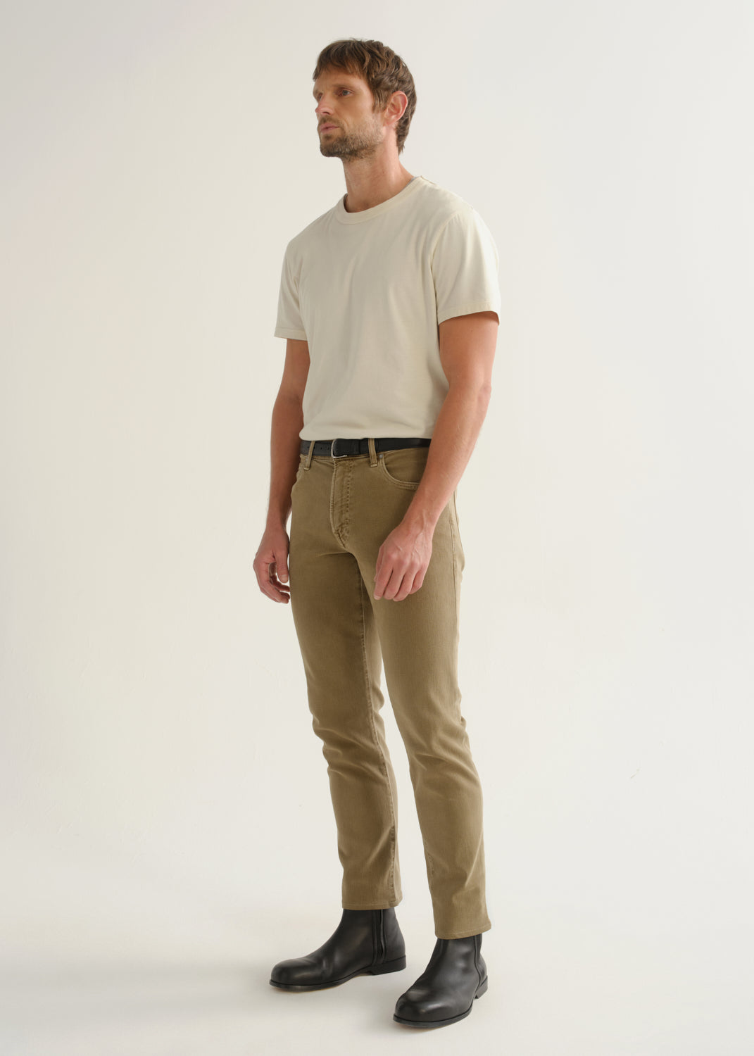Person wearing ecru short sleeve crewneck t-shirt with tan pants and black boots, side view.