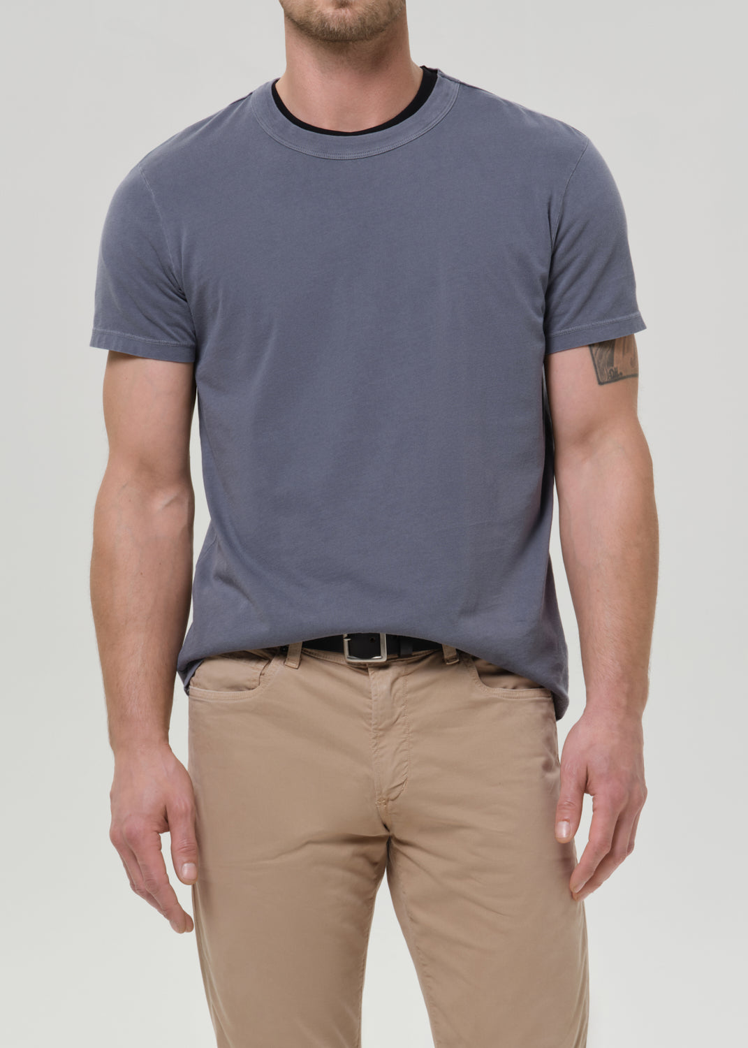 Man wearing a gray t-shirt and beige pants against a plain background