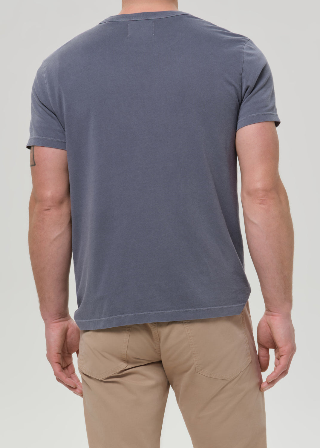 Person wearing a plain gray t-shirt and beige pants on a light gray background
