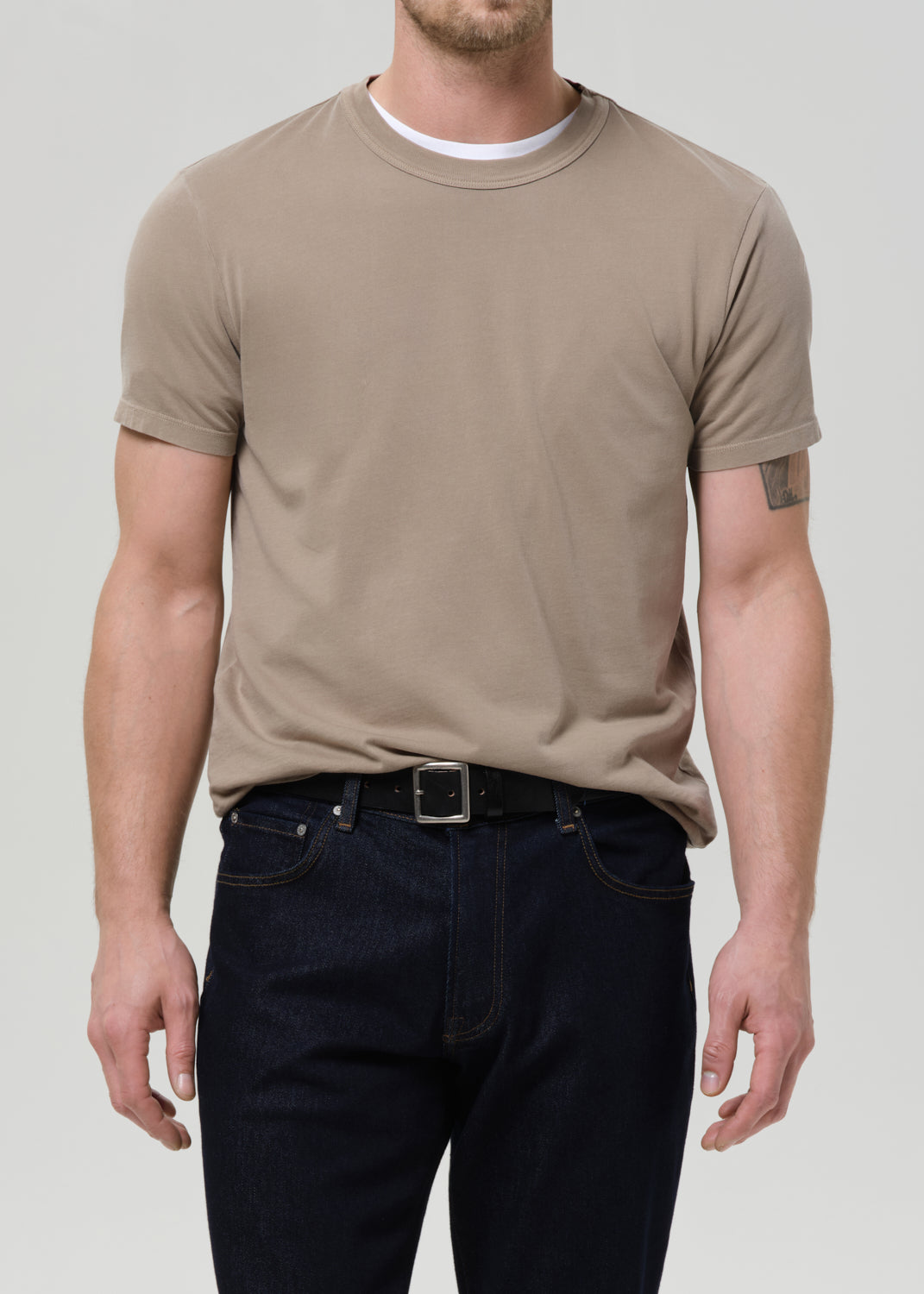 Man wearing a beige t-shirt and dark jeans on a plain background