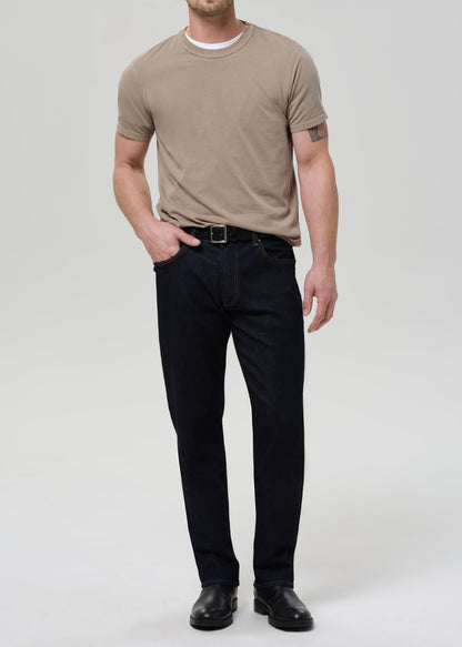 Man wearing a beige t-shirt and dark jeans on a grey background