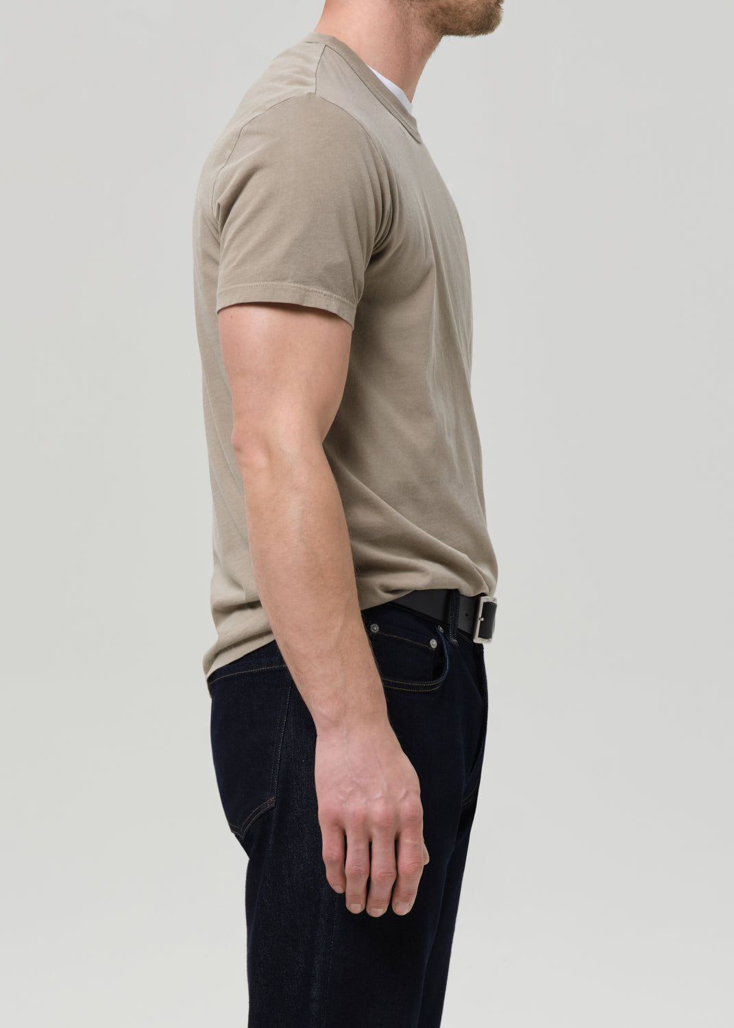 Man wearing a beige polo shirt and dark jeans on a light gray background