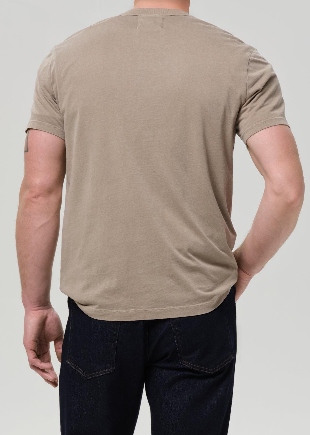 Person wearing a beige t-shirt and dark pants on a plain background