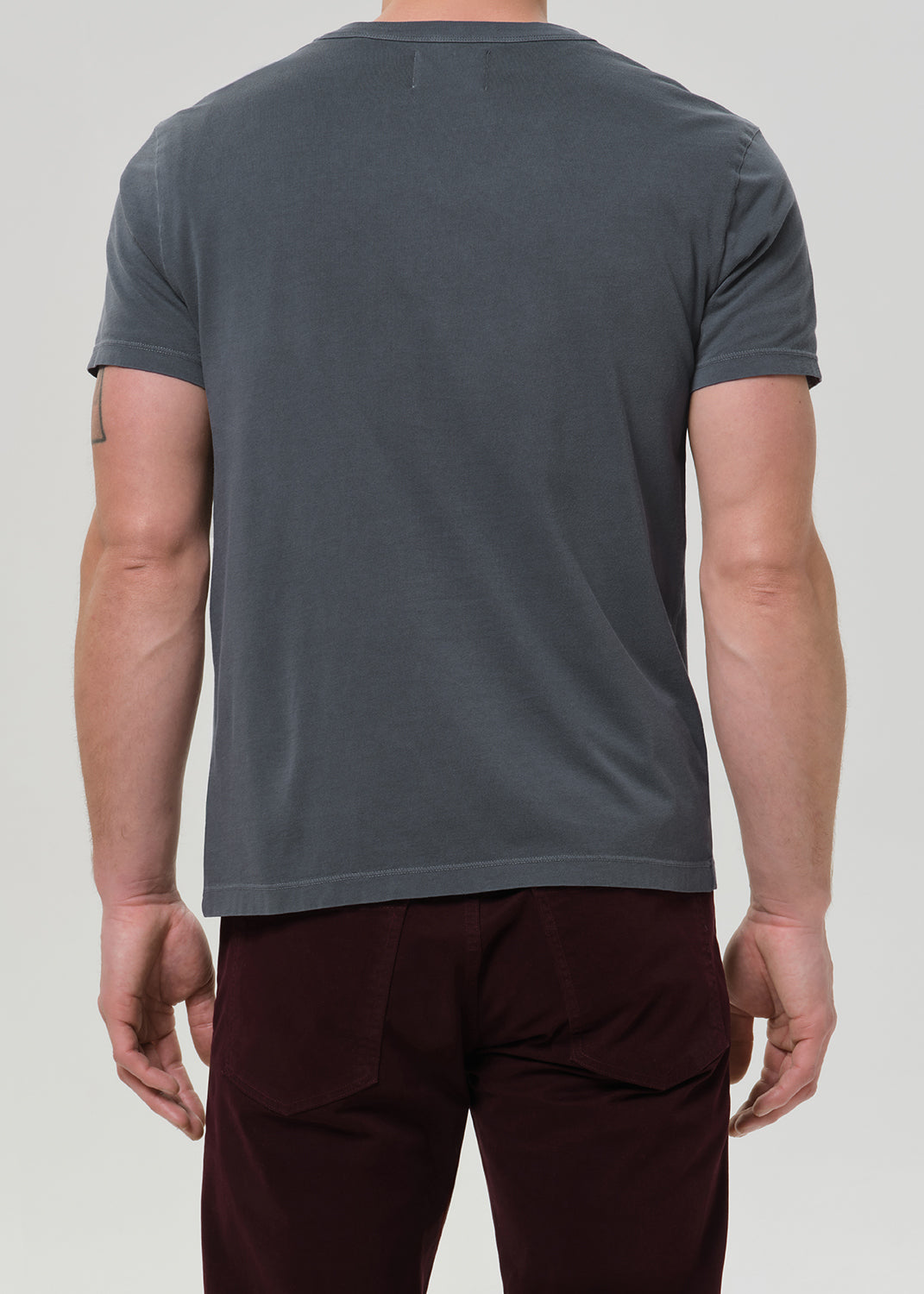 A man modeling a dark gray crewneck t-shirt and dark burgundy corduroy trousers, paired with black leather boots, against a plain light gray studio background.