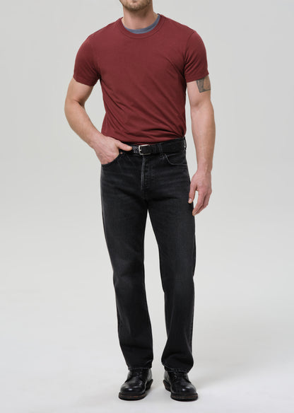 Man wearing a red t-shirt and black jeans on a grey background
