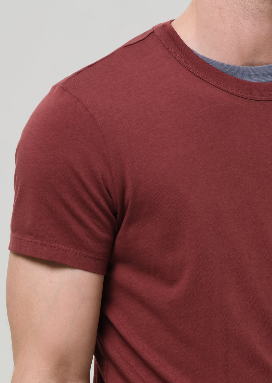 Close-up of a person wearing a maroon t-shirt against a grey background