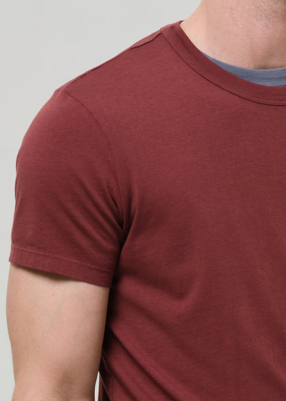 Close-up of a person wearing a maroon t-shirt against a grey background