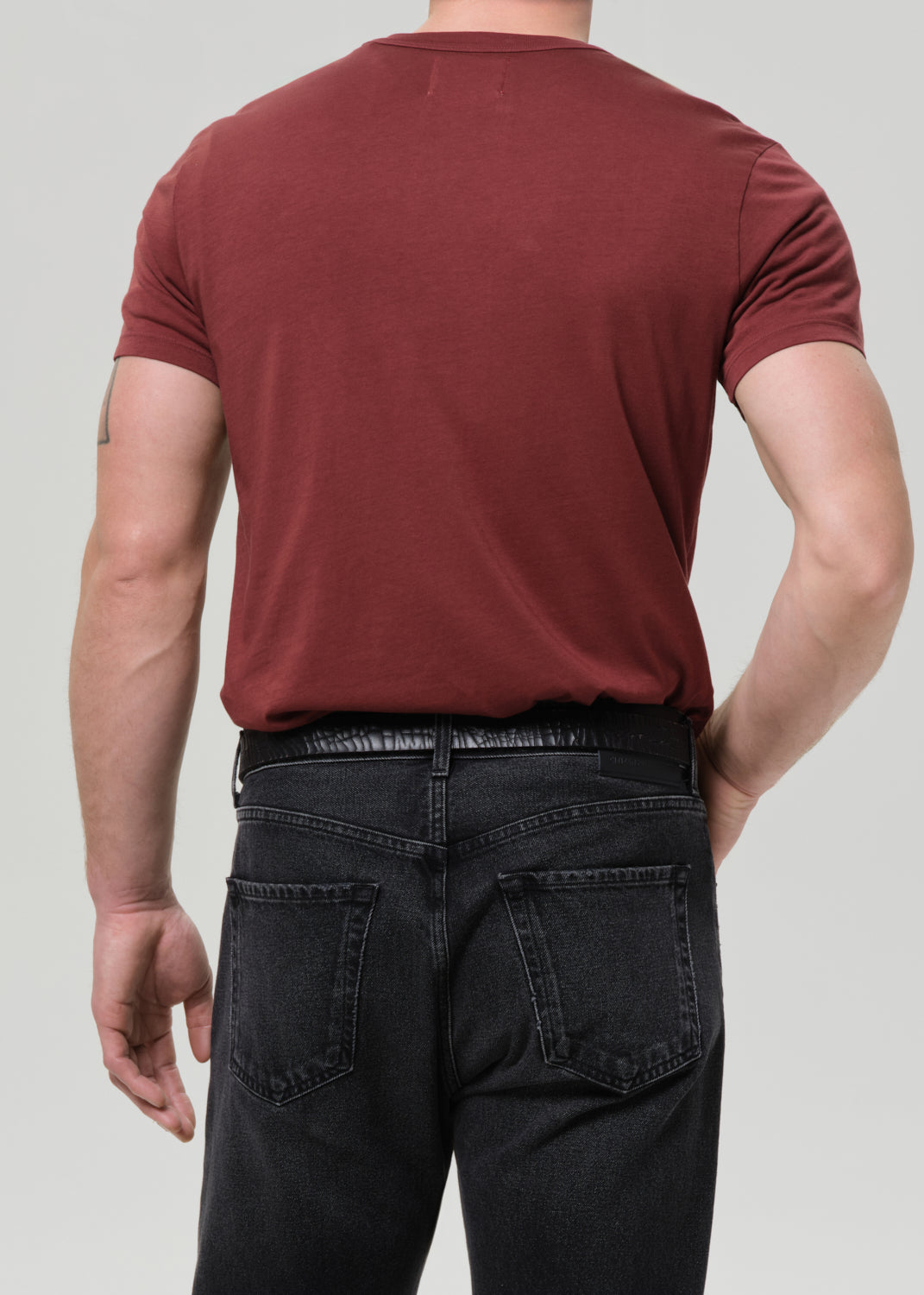 Person wearing a maroon t-shirt and black pants on a grey background