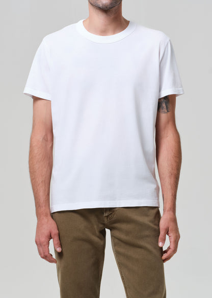 Person wearing a plain white t-shirt and brown pants on a neutral background