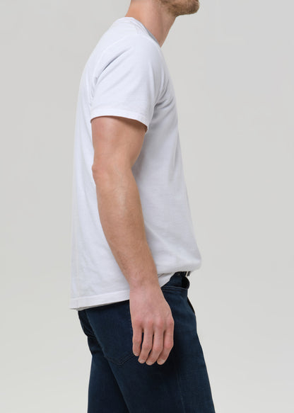 A man shown from the side wearing a plain white short-sleeve crew-neck t-shirt and dark blue jeans, photographed against a grey background.