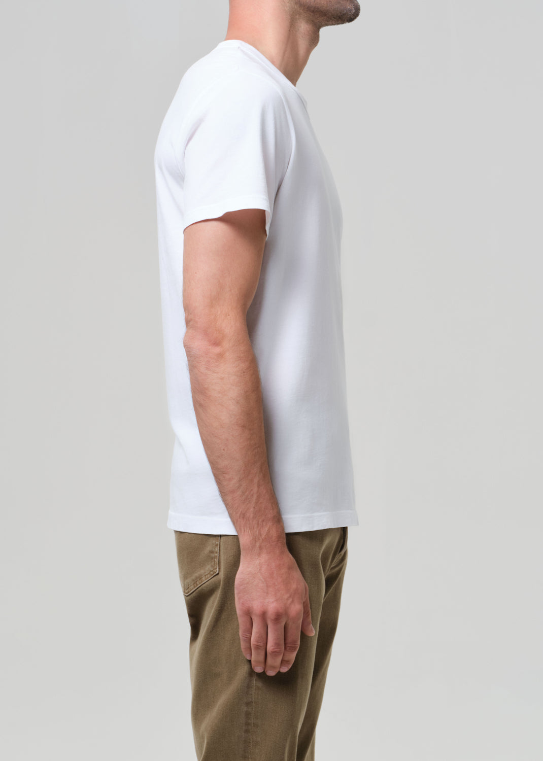 Person wearing a plain white t-shirt and brown pants on a light gray background