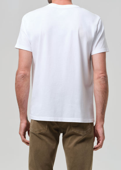 Person wearing a plain white t-shirt and brown pants on a light gray background