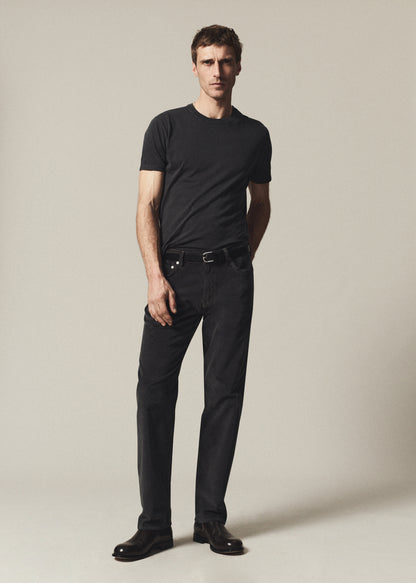Man wearing a washed black short sleeve crewneck tee with black straight leg jeans on a grey background.
