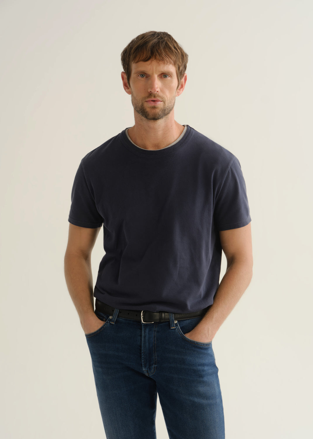 Person wearing a dark charcoal short sleeve crewneck t-shirt with blue jeans, front cropped view on a light grey background.