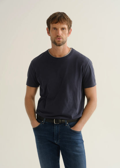 Person wearing a dark charcoal short sleeve crewneck t-shirt with blue jeans, front cropped view on a light grey background.