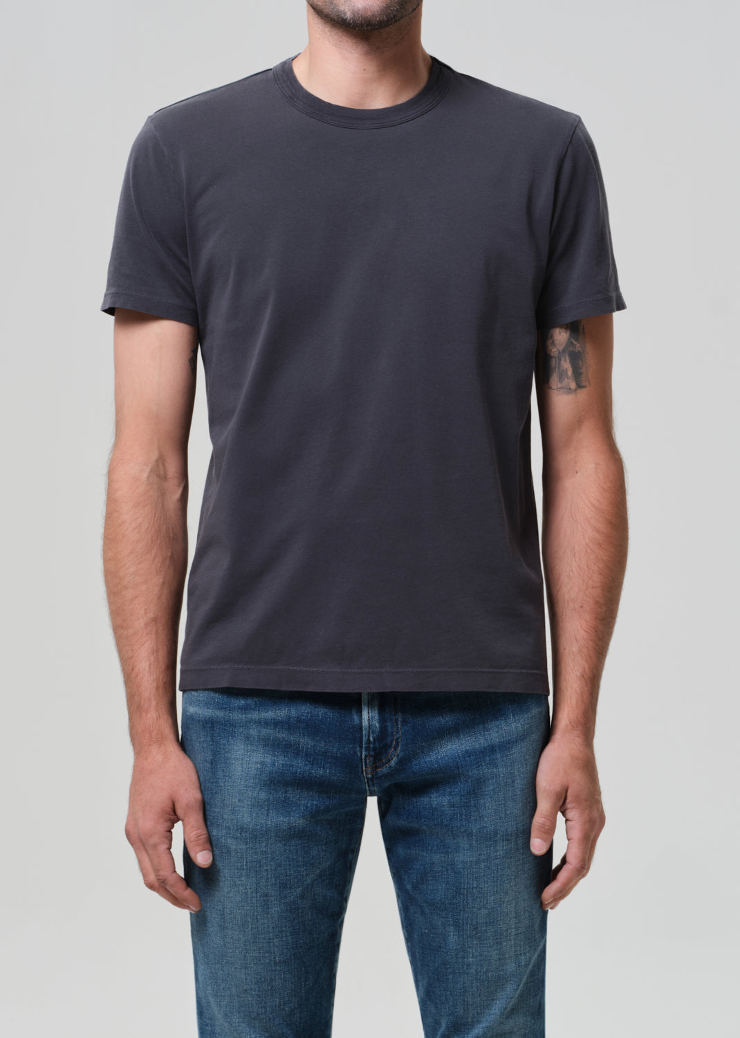 Person wearing a plain grey t-shirt and blue jeans on a light gray background