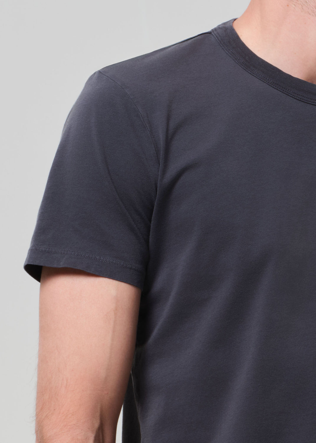 Person wearing a plain grey t-shirt and blue jeans on a light gray background