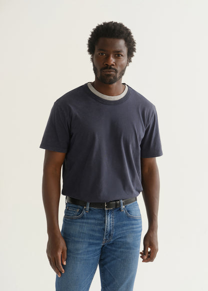 Person wearing a navy blue short sleeve crewneck t-shirt with medium blue jeans, front cropped view on a light grey background.
