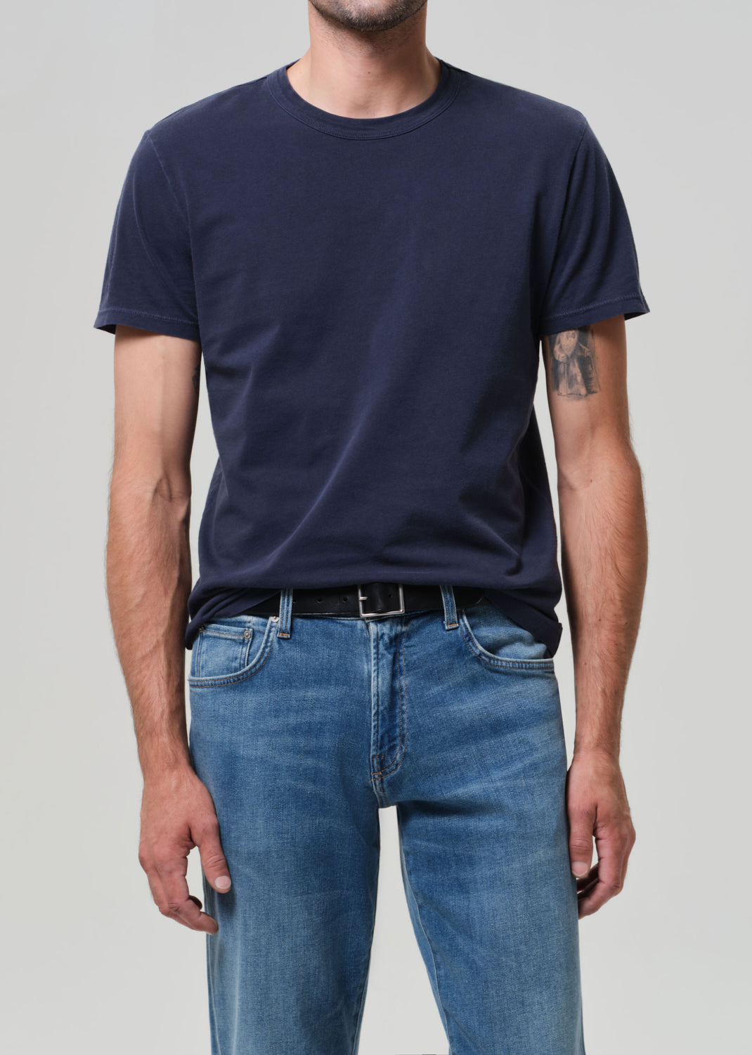 Person wearing a navy blue t-shirt and blue jeans on a plain background