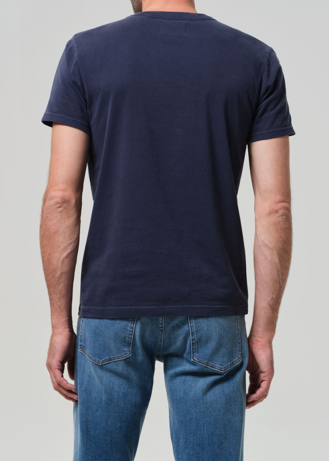 Person wearing a navy blue t-shirt and blue jeans on a light gray background
