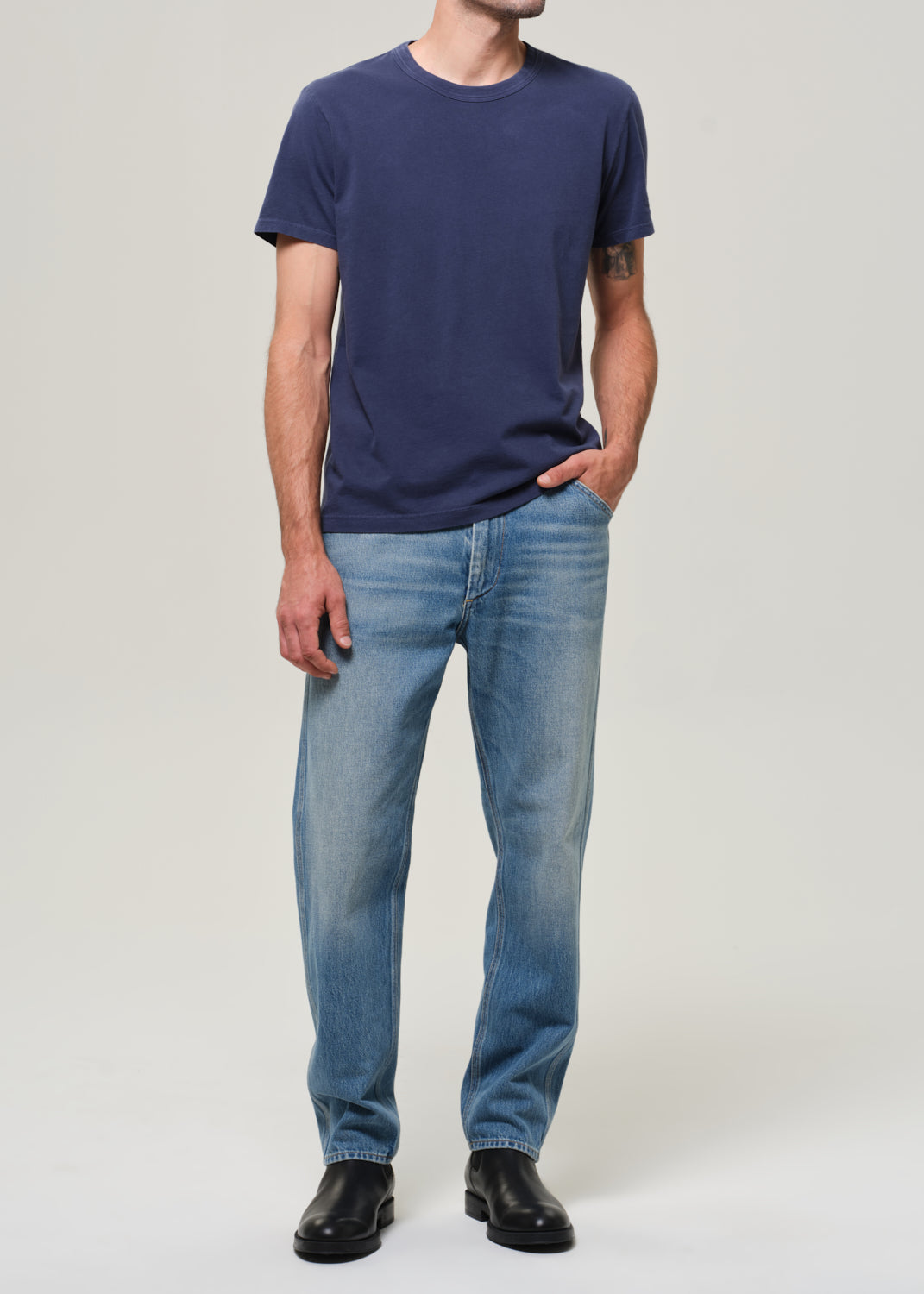 Person wearing a navy blue t-shirt and light blue jeans on a plain background
